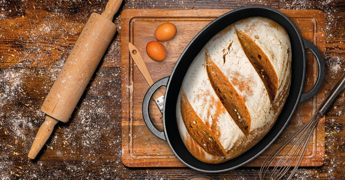 Ein Krustenzauber Gusseisen Brotbacktopf steht mit einem knusprigem Brot auf einem Tisch.